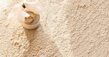 Two gold wedding rings lie on a round concrete natural podium with a white flower. Embossed sand-colored concrete background. space for text photo