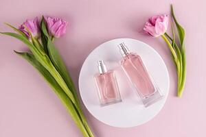 Two transparent bottles of different shapes with perfume lie on a round white podium among tulips. Beauty and perfumery concept. Top view. photo