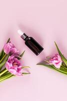 Cosmetic product, serum, oil for face and body skin care in a dark glass bottle with a dropper. Top vertical view. Spring flowers. photo