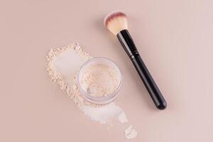 Glass jar with loose powder, swatch powder and makeup brush, applying powder on face on beige background. Concept of cosmetics , makeup. Top view. photo