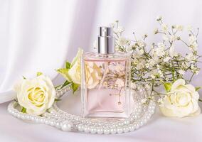 A chic bottle of women's perfume with a floral delicate fragrance on a white satin background with pearl beads. Front view. Product presentation. photo