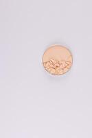 A compact powder in a natural beige color in a round block with broken pieces of texture. Top view. Vertical white background. layout. A copy space. photo