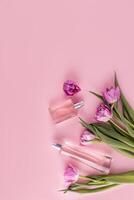 Two glass different bottles with cosmetic spray or perfume on a pink background among tulips. Vertical top view. Flat lay. A copy space. photo