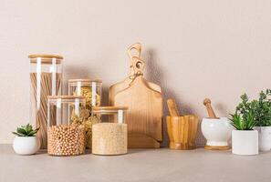A set of glass jars with bulk products, cutting boards, , potted plants on kitchen countertop. Eco-friendly materials. Eco tableware. Front view photo