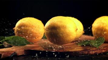 A ripe lemon falls on a cutting board with splashes of water. On a black background. Filmed is slow motion 1000 fps. video