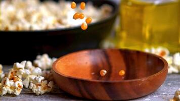 Popcorn is being transferred from a bag into a wooden bowl on a table. The snack is ready to be enjoyed with a drink or while watching a movie video