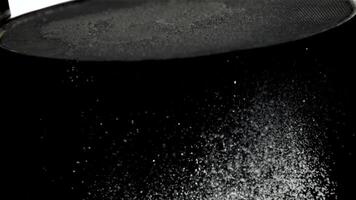 A mesmerizing of powdered sugar and flour being sifted through a sieve on a black surface, creating a beautiful contrast video