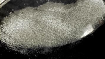 A closeup monochrome photograph of a pile of white powder on a dark surface resembling soil or rock, creating a stark contrast in darkness and light video