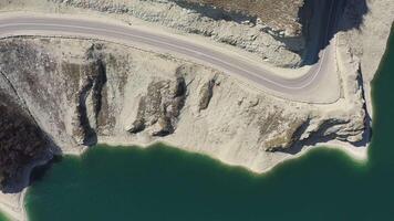 Drohne oben runter. Berg Straße Winde entlang ein hoch Cliff auf das Ufer von ein See video