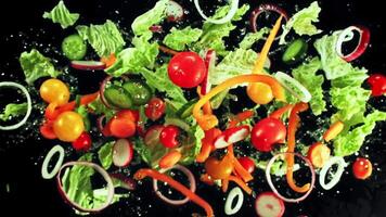 un' fresco insalata fatto con lattuga, pomodori, peperoni, cipolle, e altro la verdura, tutti visualizzato su un' elegante nero sfondo per evidenziare loro naturale colori e textures video