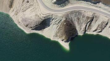 Antenne oben runter. Berg Straße Winde entlang ein hoch Cliff auf das Ufer von ein See video