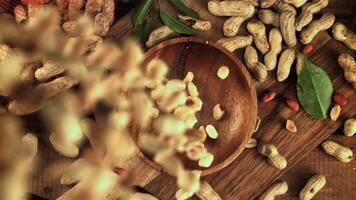 Peeled peanuts fall into the plate. On a wooden background. Top view.Filmed is slow motion 1000 frames per second. High quality FullHD footage video