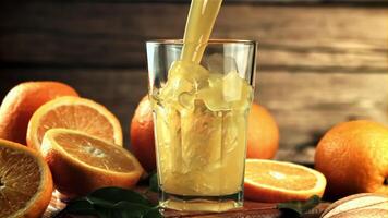 A stream of orange juice pours into the glass in a whirlpool. On a wooden background. Filmed is slow motion 1000 frames per second. video