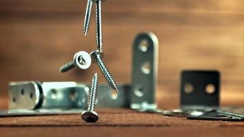 A bunch of self-tapping screws fall on the table. On a wooden background.Filmed is slow motion 1000 fps. High quality FullHD footage video