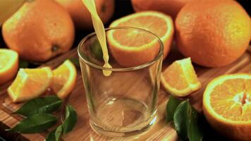 ein Strom von Orange Saft gießt in das Glas im ein Whirlpool. auf ein hölzern Hintergrund. gefilmt ist schleppend Bewegung 1000 Frames pro zweite. video