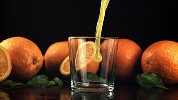 A stream of orange juice with splashes pours into the glass. On a black background. Filmed is slow motion 1000 fps. High quality FullHD footage video