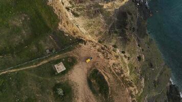 A yellow car stands on the edge of a cliff at Cape Lermontov. Drone view video