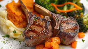 Roasted lamb chops with a side of mashed sweet potato and steamed vegetables. The steamed vegetables are a mix of broccoli and carrots. photo