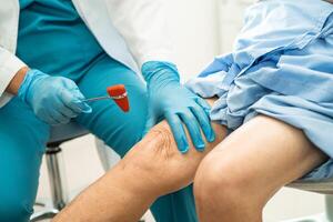 Asian doctor use hammer knock senior woman patient to check knee reflex, nerve and muscle in hospital. photo