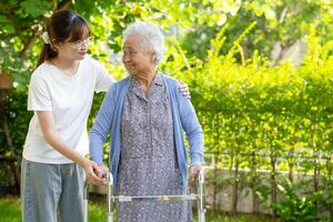 Caregiver help Asian elderly woman patient walk with walker in park, healthy strong medical concept. photo