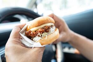 asiático dama participación hamburguesa a comer en auto, peligroso y riesgo un accidente. foto