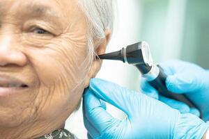 audiólogo o ent médico utilizar otoscopio comprobación oído de asiático mayor mujer paciente tratando escuchando pérdida problema. foto
