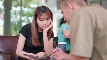 A man talks and presents a project to a colleague using a tablet at a cafe. video