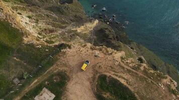 A yellow car stands on the edge of a cliff at Cape Lermontov. Drone view video