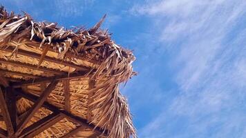 Footage of the beach umbrella made of the palm tree leaves with blue sky and clouds on the background. Travel video