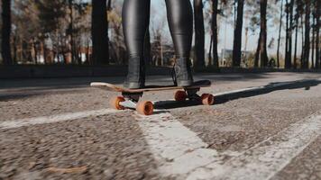 Close-up of a young girl skillfully speeding along on a skateboard on an asphalt path of a city park on a sunny day, back view. Concept of interesting autumn urban leisure video