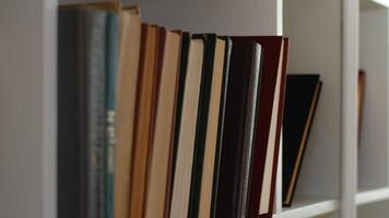 Person vorsichtig nehmen ein Buch von das Reihe Stehen auf ein Regal von ein Weiß Bücherregal beim Zuhause schließen hoch. Konzept von Neugierde im Bildung und Durst zum Wissen video