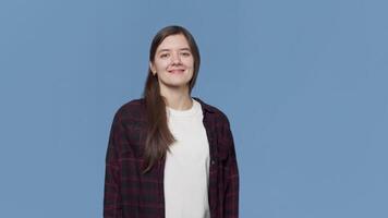 portrait de une Jeune attrayant souriant femme permanent et à la recherche à le caméra avec une content positif visage sur une bleu Contexte dans le studio video