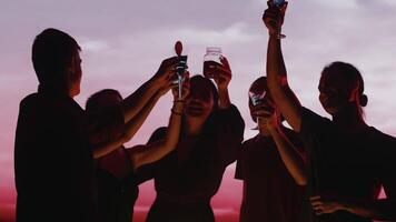 Jeune copains élevage mains avec cocktails, tintement leur des lunettes et dansant permanent dans le cercle dans un Extérieur fête avec une rouge crépuscule ciel dans le toile de fond. concept de insouciant été amusement video