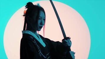 Young asian woman in a traditional kimono with a raised katana standing still in the studio with a turquoise blue green background and red sun close up video