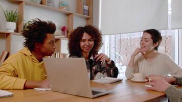 Young woman explaining with enthusiasm work project details to multiracial corporate employees team and laughing while sitting together in office on the common table with laptop video