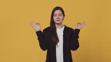 jovem atraente mulher meditando em uma amarelo fundo dentro uma estúdio. atento, calma e relaxado mulher conectando a polegar e indicador em ambos mãos, colocando eles para a lados e sorridente video