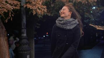 jung glücklich attraktiv Frau im ein Mantel und Schal fröhlich überspringen auf das Bürgersteig im das Abend Stadt Straße und lächelnd. Konzept von gemütlich und komfortabel Herbst städtisch Leben video