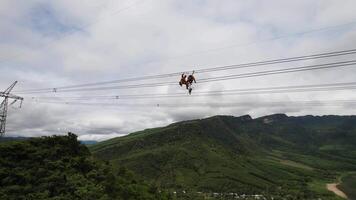 High angle view of an adventurous person performing an exhilarating zipline activity over a lush green valley, illustrating outdoor sports and adventure tourism video