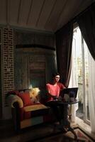 Villa Relaxation, Asian Model Working on Laptop, Basking in Sunlit Comfort photo