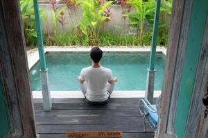 junto a la piscina serenidad, asiático modelo en loto yoga pose, bali villa relajación foto