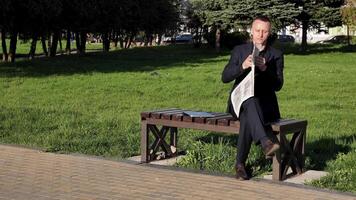 A young seriously businessman in a business suit holds and reading a paper newspaper The New York Times outside in a park. Summer, sunny video