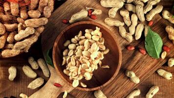 Peeled peanuts fall into a plate. On a wooden background. Top view. Filmed is slow motion 1000 frames per second. High quality FullHD footage video