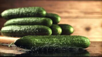 un Fresco Pepino caídas en el mesa con salpicaduras de agua. en un de madera antecedentes. filmado es lento movimiento 1000 marcos por segundo. video