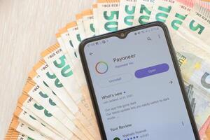 TERNOPIL, UKRAINE - AUGUST 3, 2023 Payoneer application on screen on modern smartphone and many bills of euro currency photo