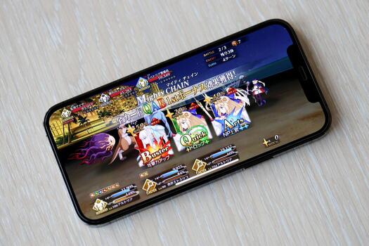 Fate Grand Order mobile iOS game on iPhone 15 smartphone screen on wooden table during mobile gameplay photo