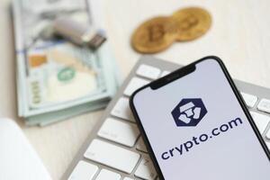 KYIV, UKRAINE - MARCH 15, 2024 Crypto com logo on iPhone display screen on white keyboard with money and bitcoins photo