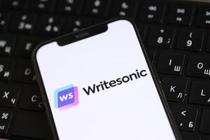 KYIV, UKRAINE - MARCH 17, 2024 Writesonic logo on iPhone display screen and MacBook keyboard photo