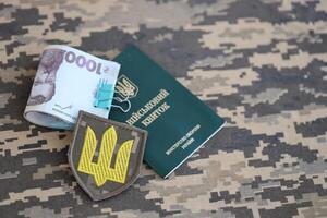 Symbol of Ukrainian army and military ID with bunch of money on the camouflage uniform of a Ukrainian soldier. Concept of payment to military personnel or bribe for deferment from service photo