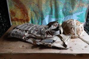 A military helmet of a Ukrainian soldier with a heavy bulletproof vest on wooden table in checkpoint dugout photo