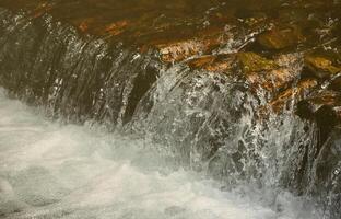 A small waterfall. The height difference of the water flow in the river is equipped with round wooden logs photo